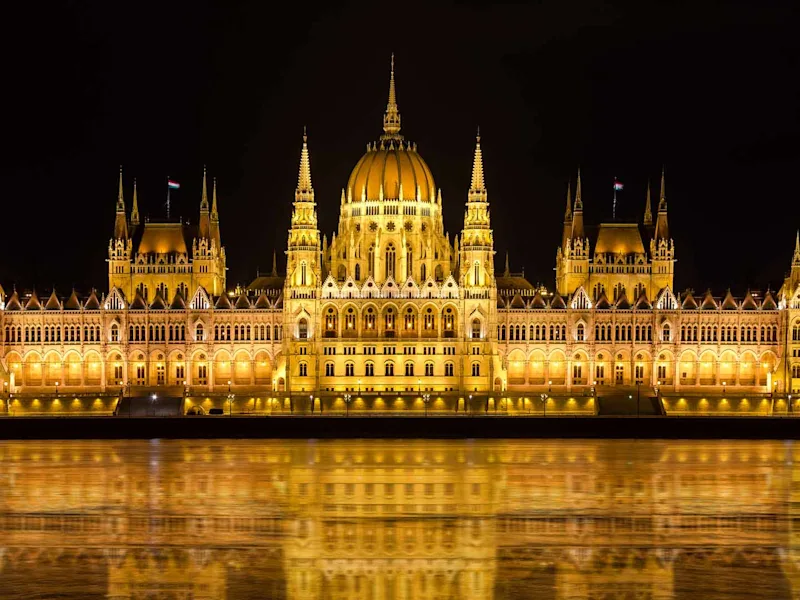 Illuminated Budapest parliament building at night with dark sky and reflection in Danube river